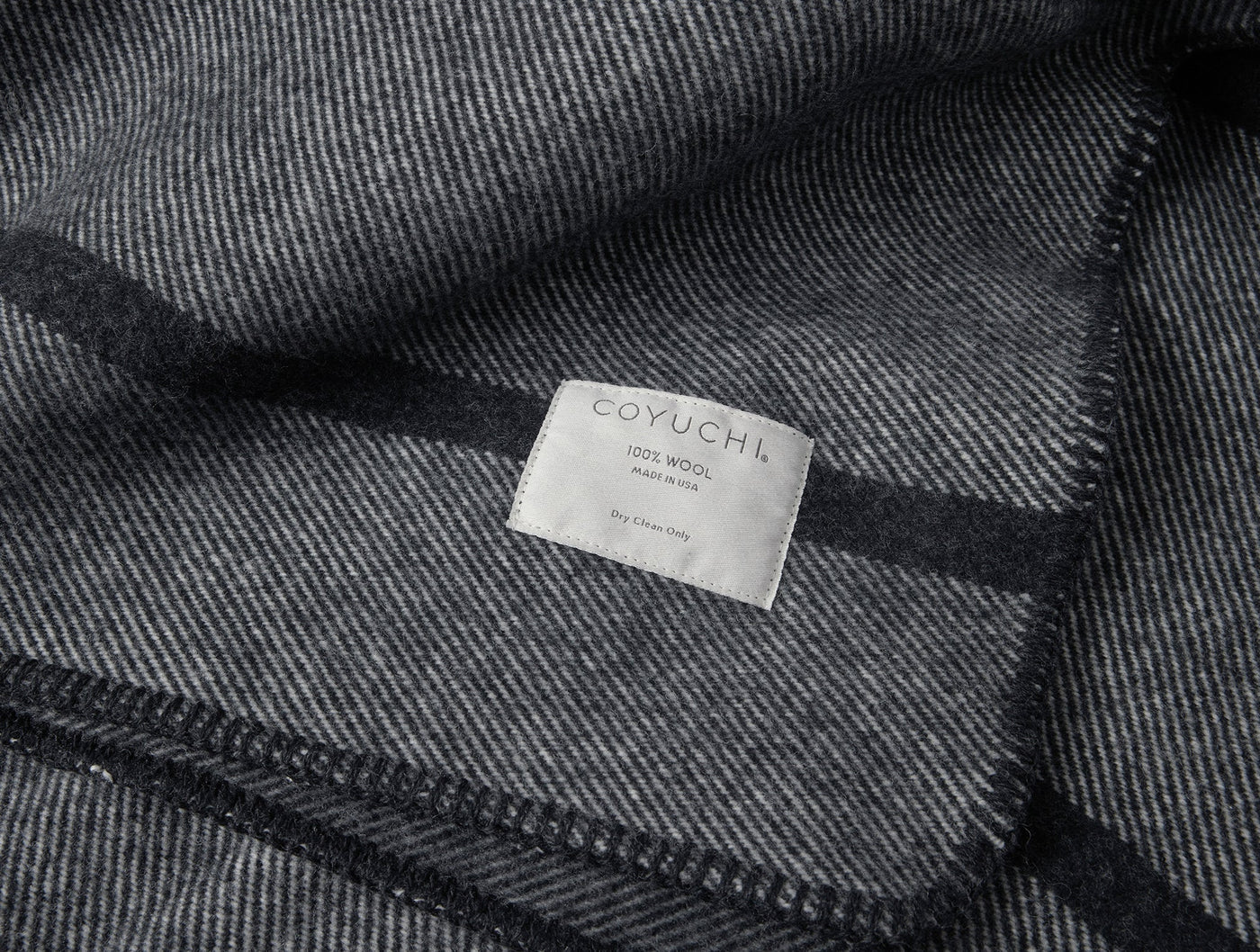 Close-up of Coyuchi label on charcoal herringbone wool blanket with dark stripe border.