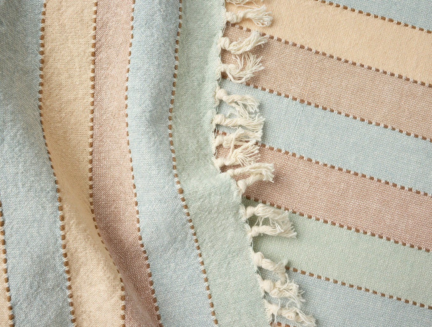 Close-up of Coyuchi Tilden napkin fringe edge detail, sage, blush, and sand stripes.