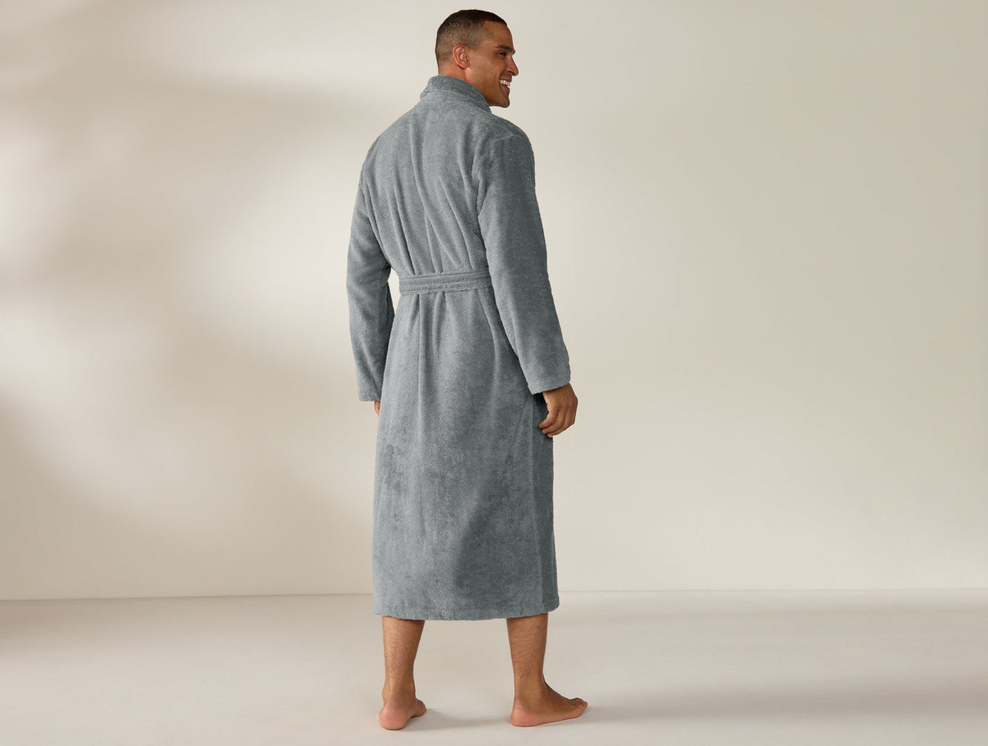 Man wearing a full-length slate Coyuchi Cloud Loom robe, back view, belted waist.