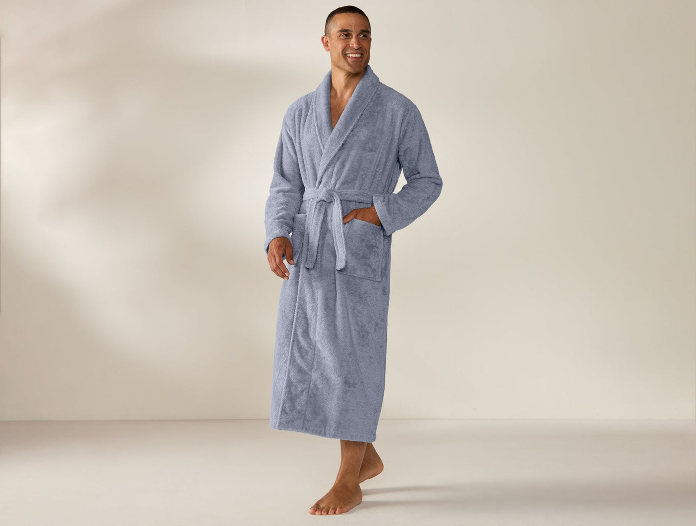 Man wearing Coyuchi Cloud Loom unisex robe in pale blue terry, full-length, belted.