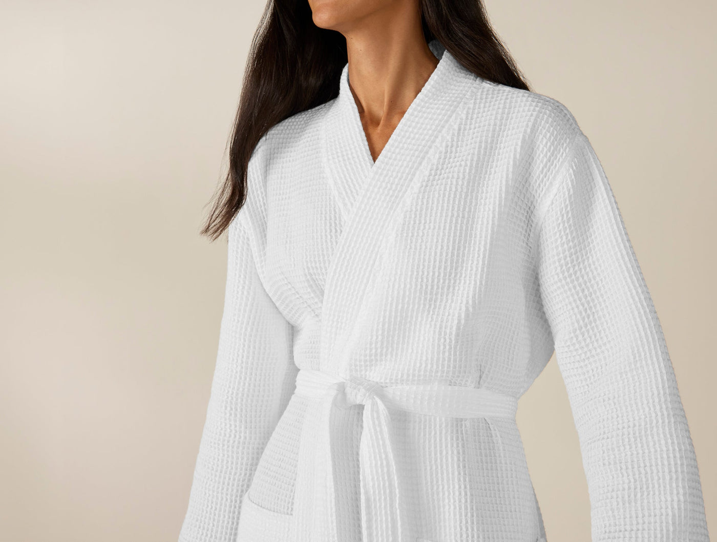 Close-up of white waffle-knit cotton robe with shawl collar and tied belt, worn on model.