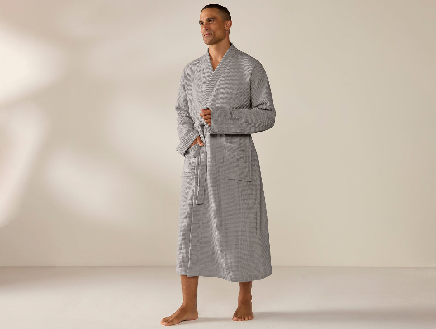 Man wearing full-length Coyuchi grey waffle robe with front pockets and belted waist.