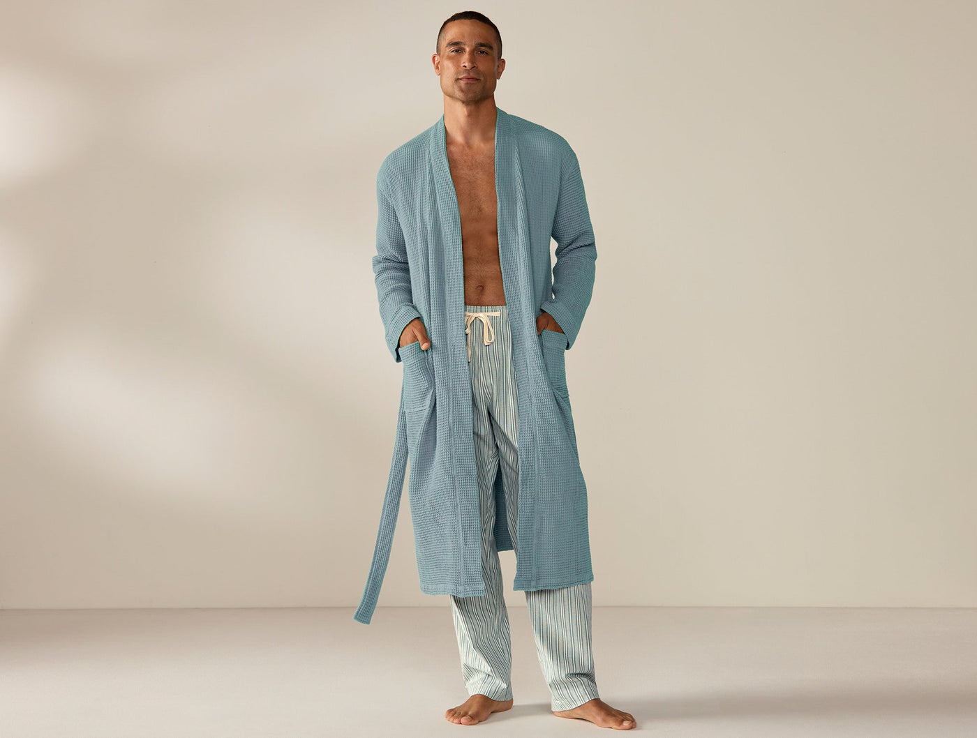 Man wearing long Coyuchi waffle robe in slate blue, open-front, full-length styling.