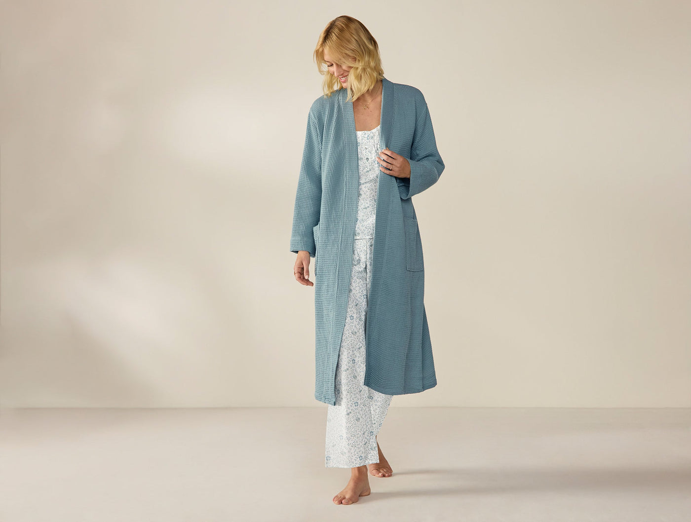 Model wearing a long slate blue waffle-texture Coyuchi robe over a floral pajama set.