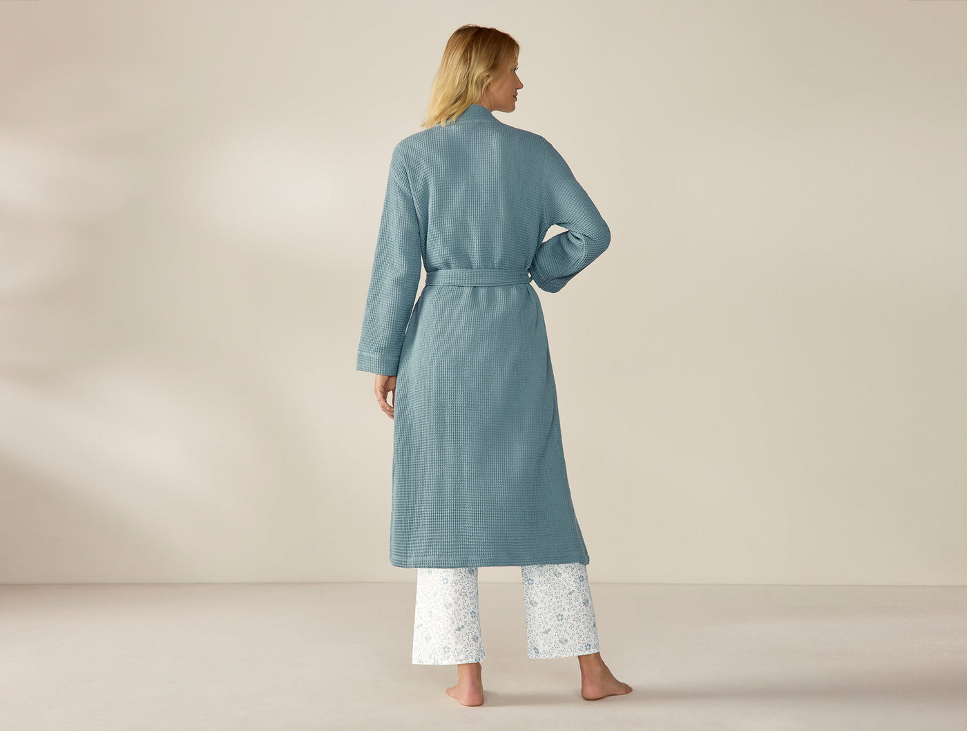 Back view of Coyuchi Unisex Waffle Robe in slate blue, belted, worn over floral pants.