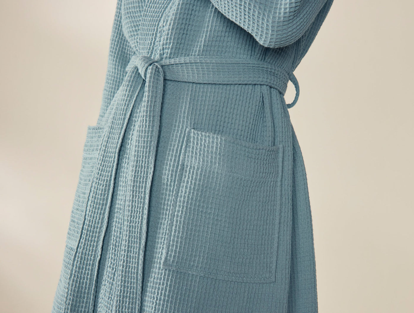 Side view of dusty blue waffle-knit robe showing belted waist and patch pocket detail.