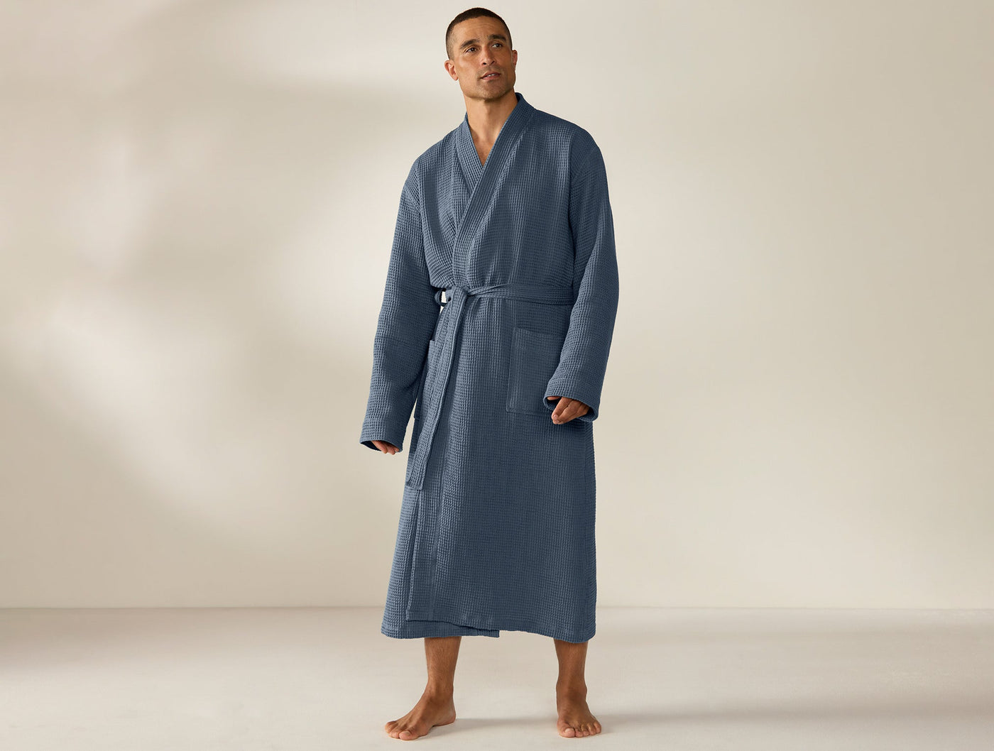 Man wearing Coyuchi Unisex Waffle Robe in slate blue, full-length front view with belt tied.