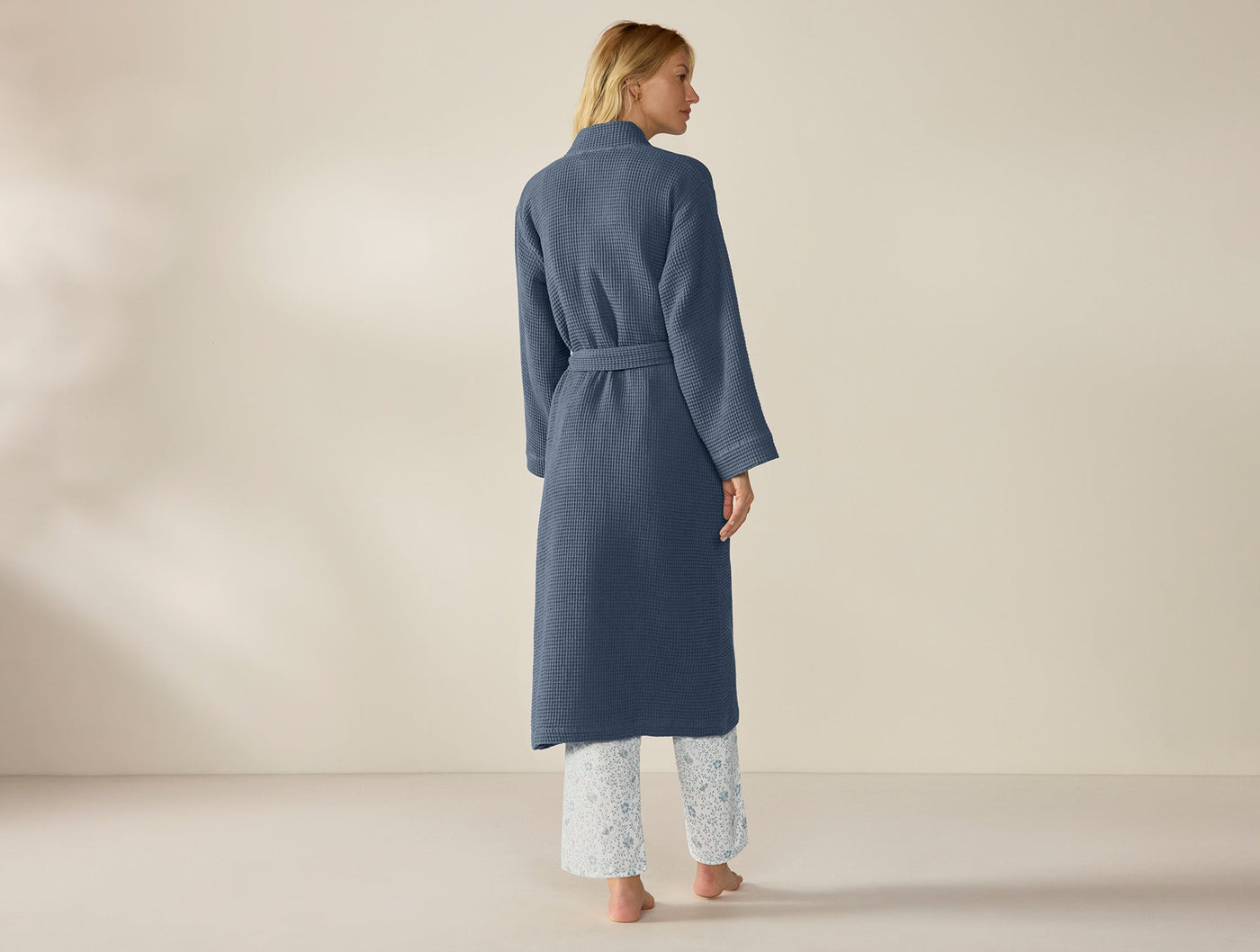 Back view of Coyuchi slate blue waffle-knit robe, belted, floor-length, worn over white pants.