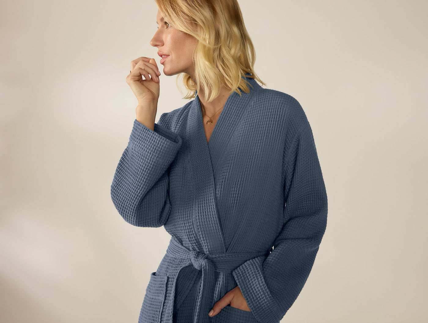 Woman wearing Coyuchi slate blue waffle-knit robe, belted at waist, close-up side view.
