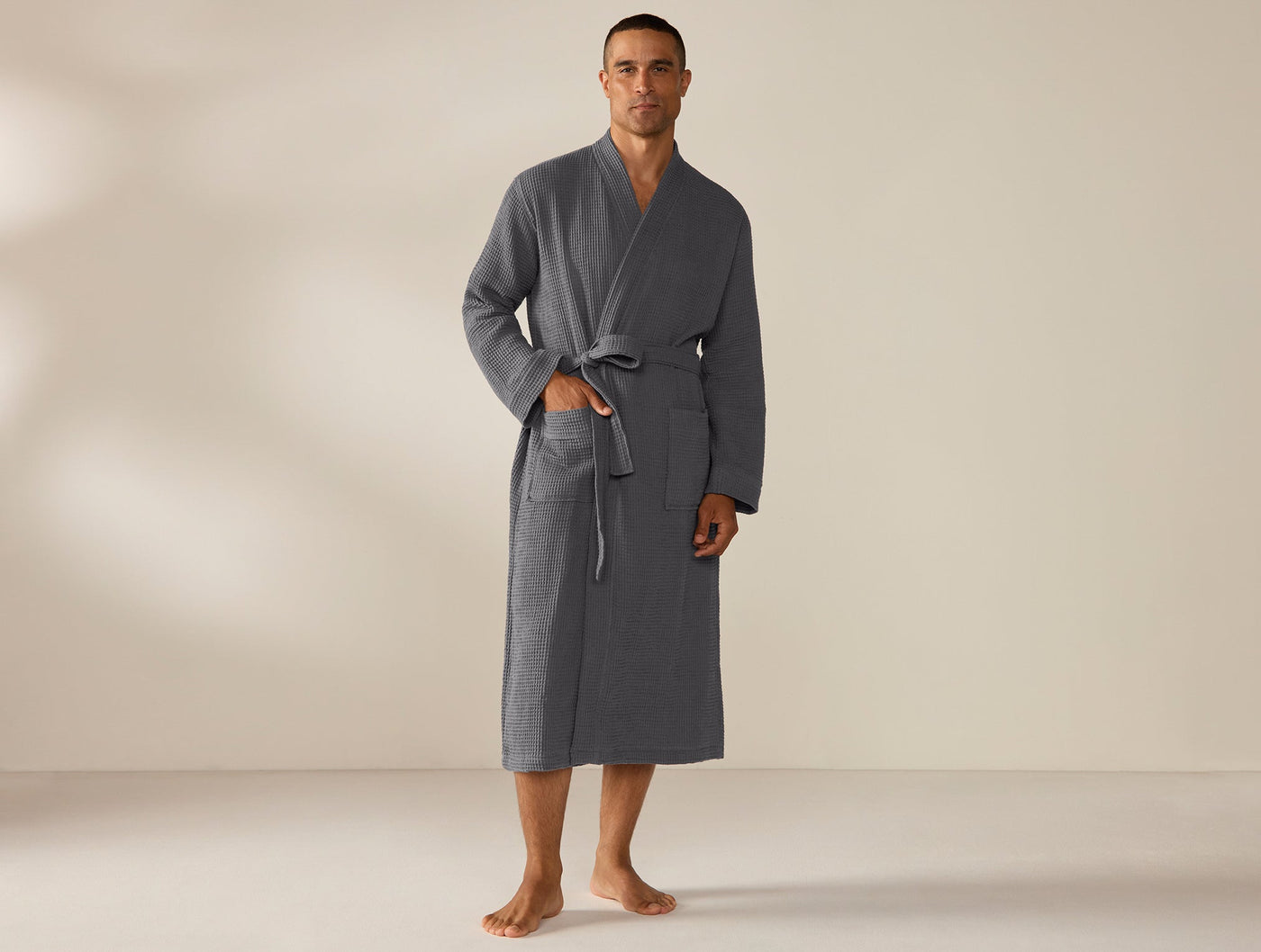 Male model wearing Coyuchi slate waffle-knit robe, belted, full-length front view.