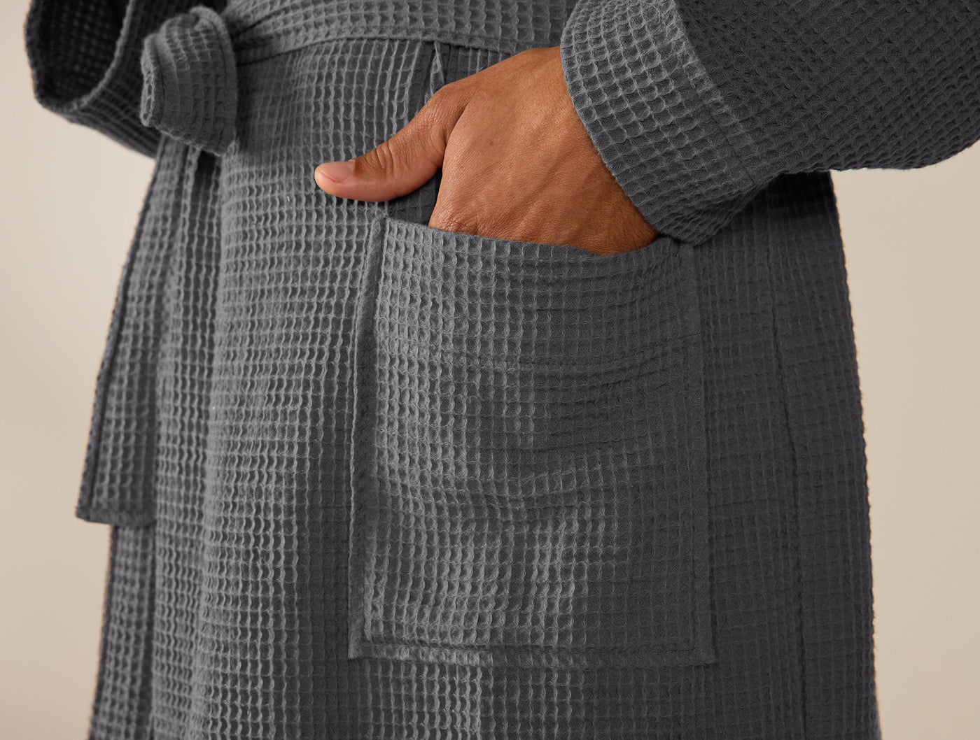 Close-up of hand in slate waffle-weave robe pocket, showing textured cotton fabric detail.