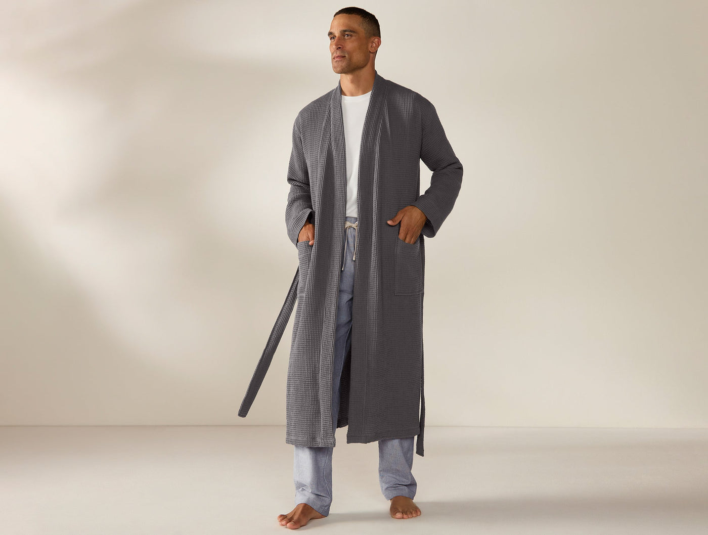 Man wearing Coyuchi slate waffle-knit long robe, open front with tie belt, patch pockets.