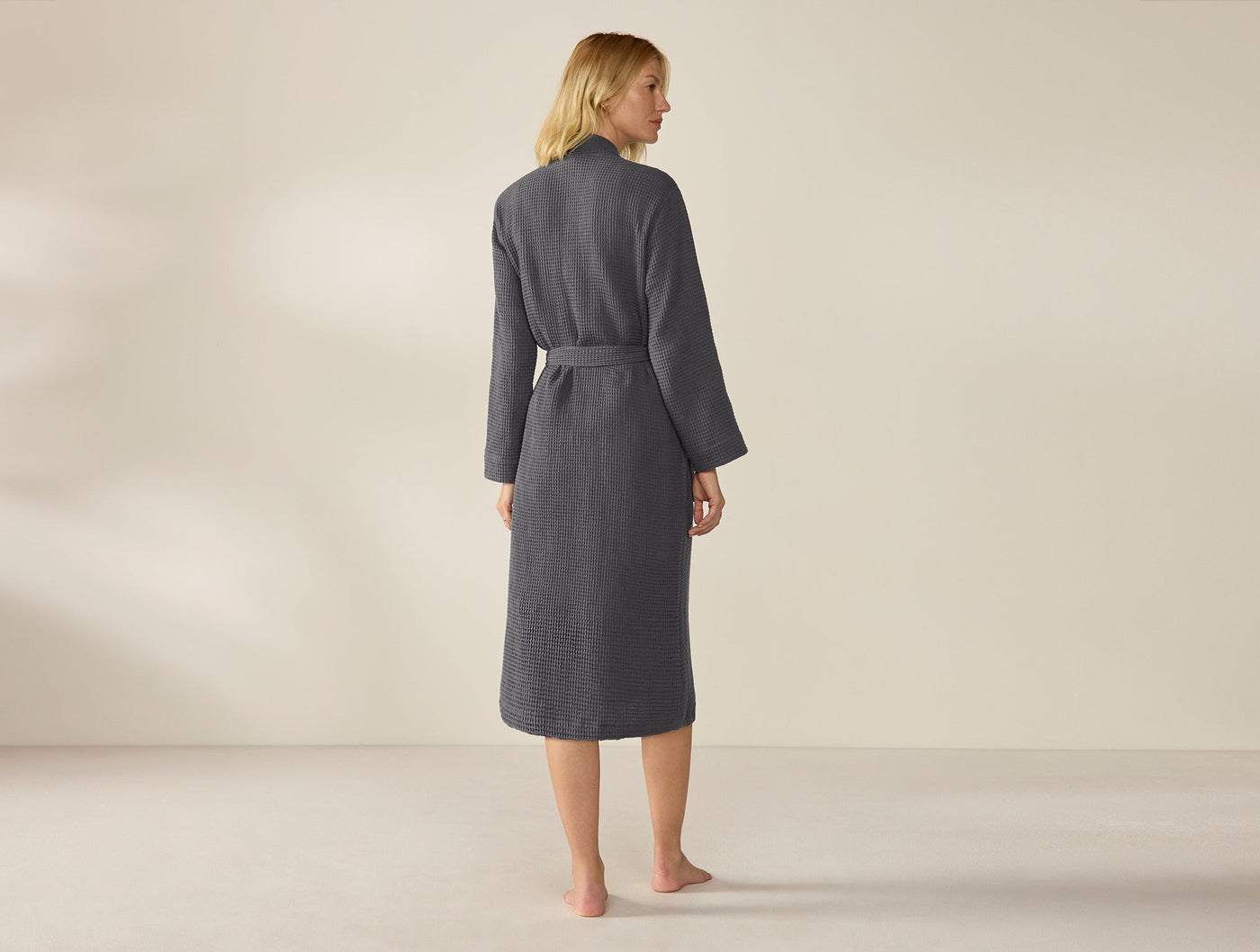 Model wearing Coyuchi slate waffle-knit robe, rear view, belted at waist, mid-calf length.