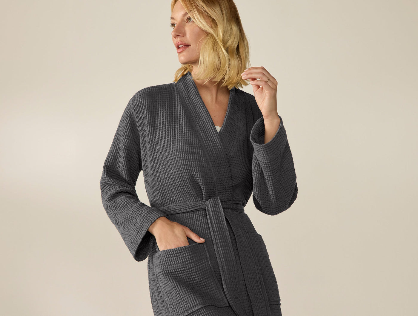 Model wearing Coyuchi waffle robe in slate, belted at waist, hand in pocket.