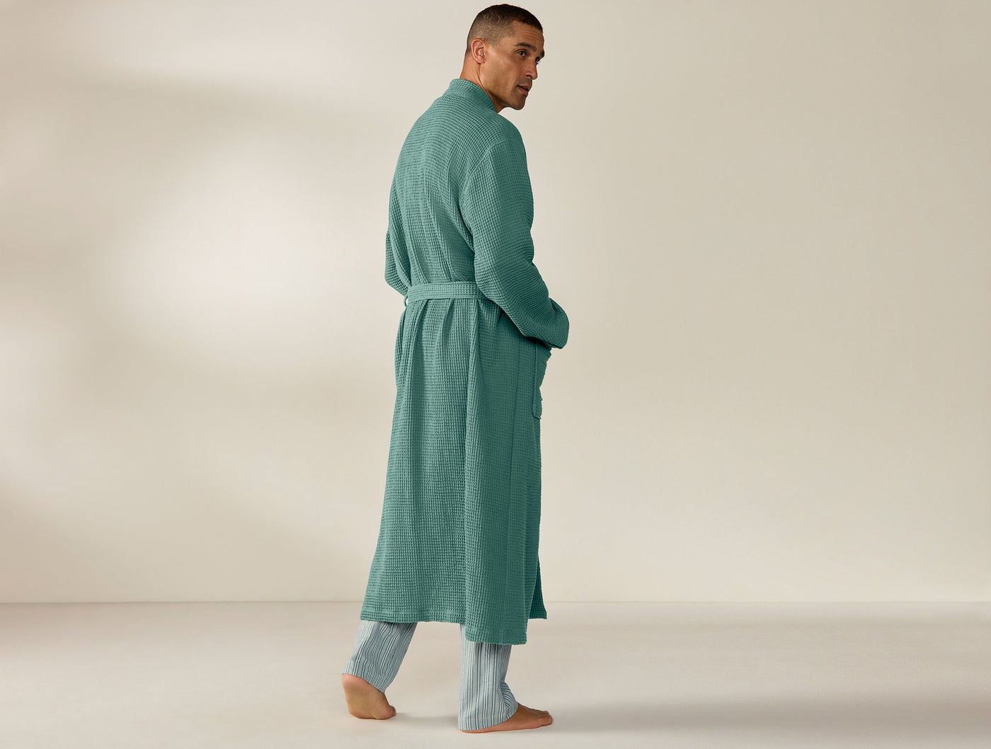 Back view of man wearing Coyuchi teal waffle-knit robe, belted, full length.