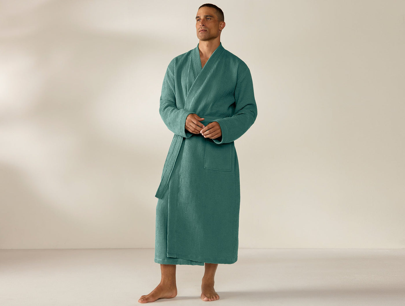 Man wearing Coyuchi teal waffle-knit robe, full-length view, belted at waist.