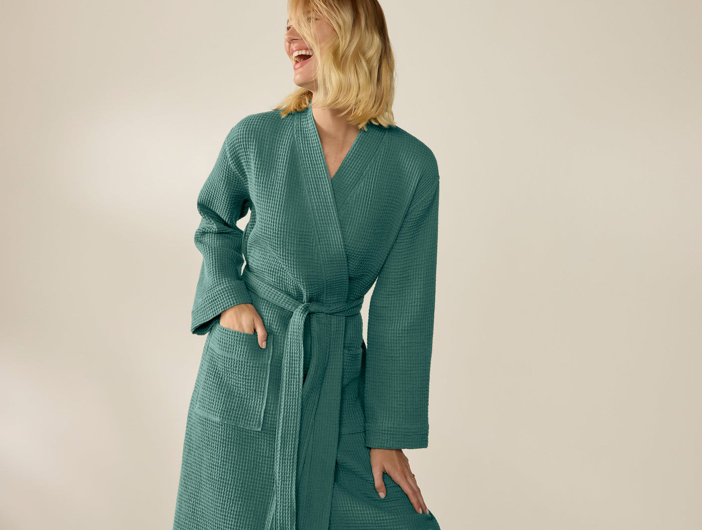 Model wearing Coyuchi teal waffle-knit robe, belted, with deep patch pockets.