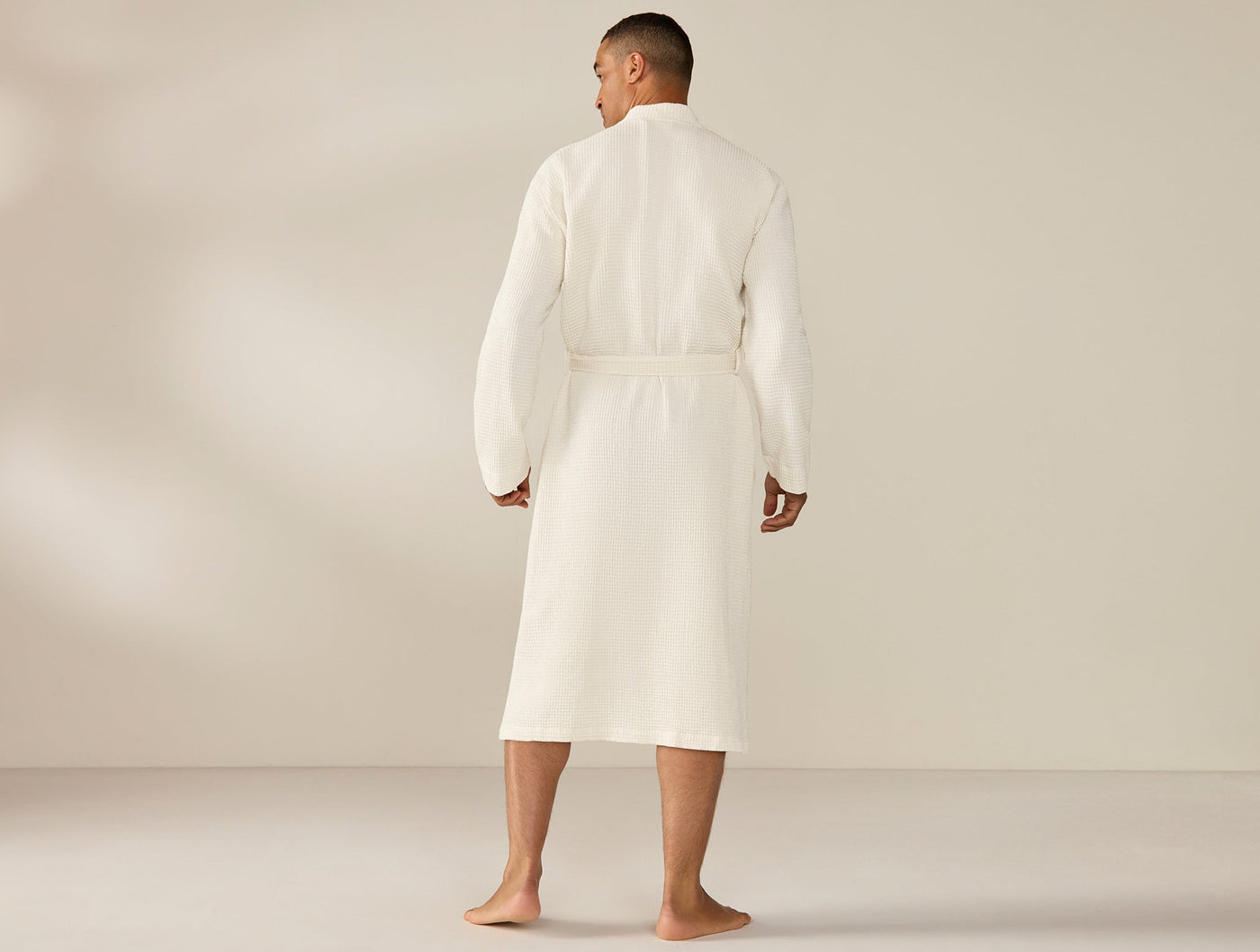 Back view of Coyuchi Unisex Waffle Robe in ivory, belted, knee-length, on male model.