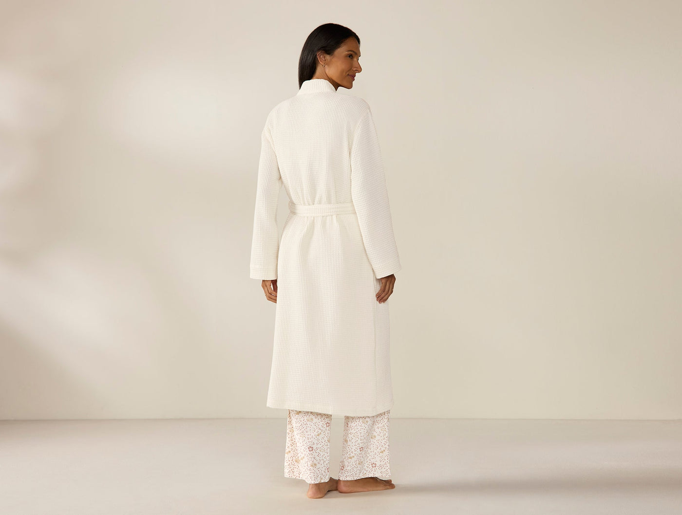 Back view of Coyuchi ivory waffle-knit robe, belted, full-length, modeled against neutral backdrop.