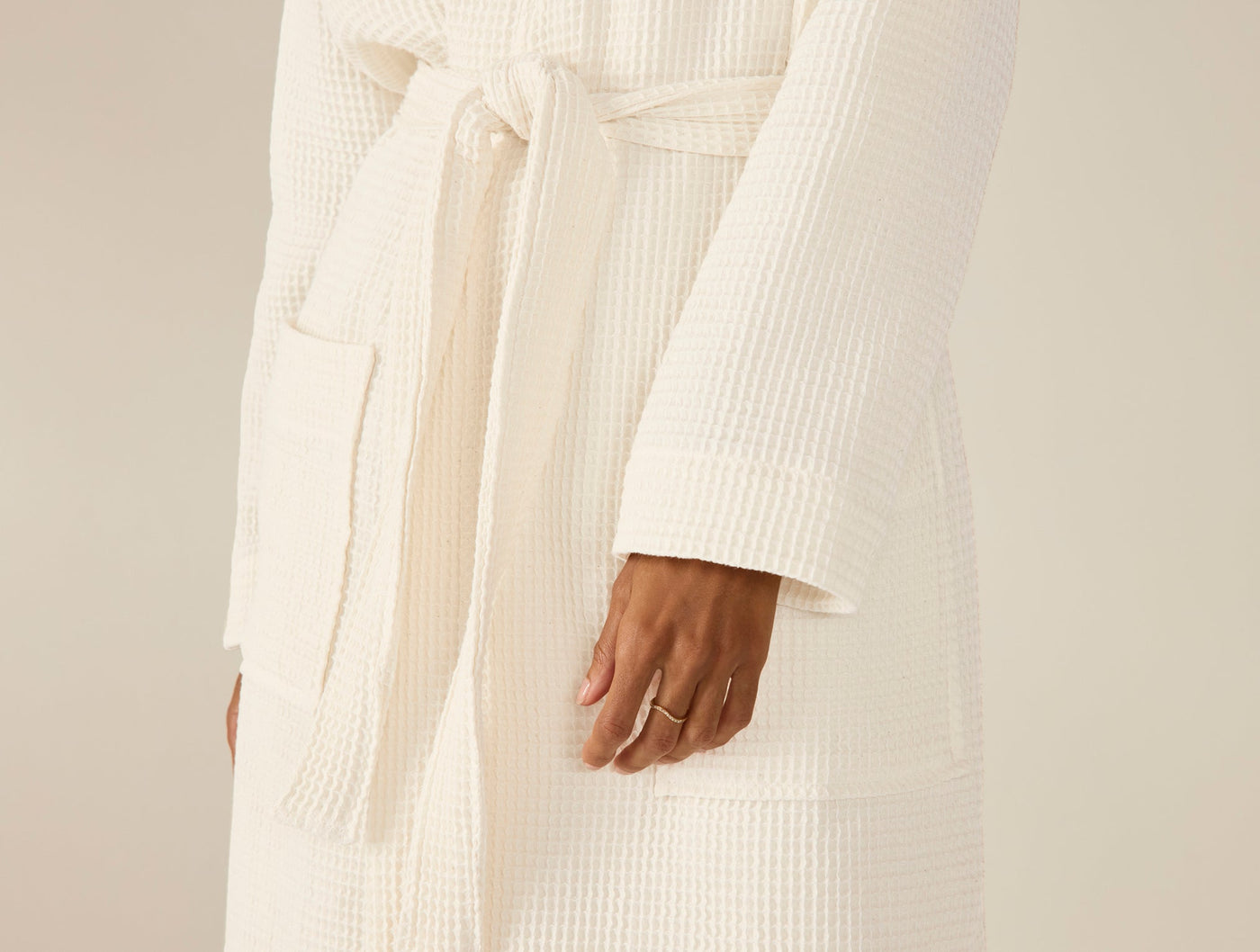 Close-up of ivory waffle-knit robe belt and pocket, hand at side.
