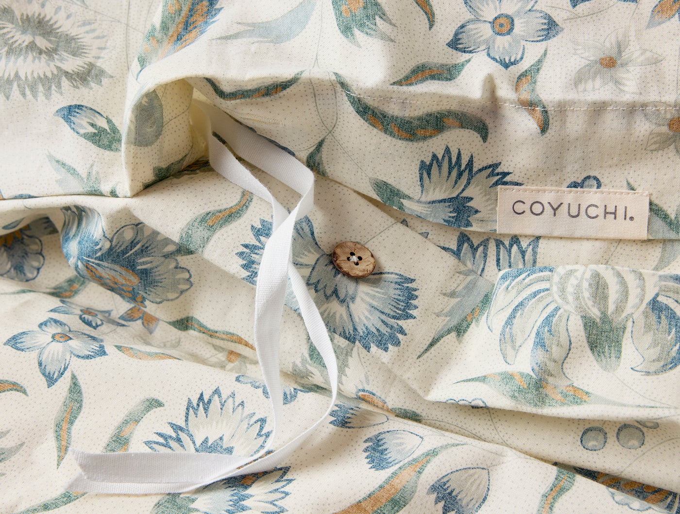 Close-up of Coyuchi Viola Print duvet cover button closure with blue floral print on ivory.