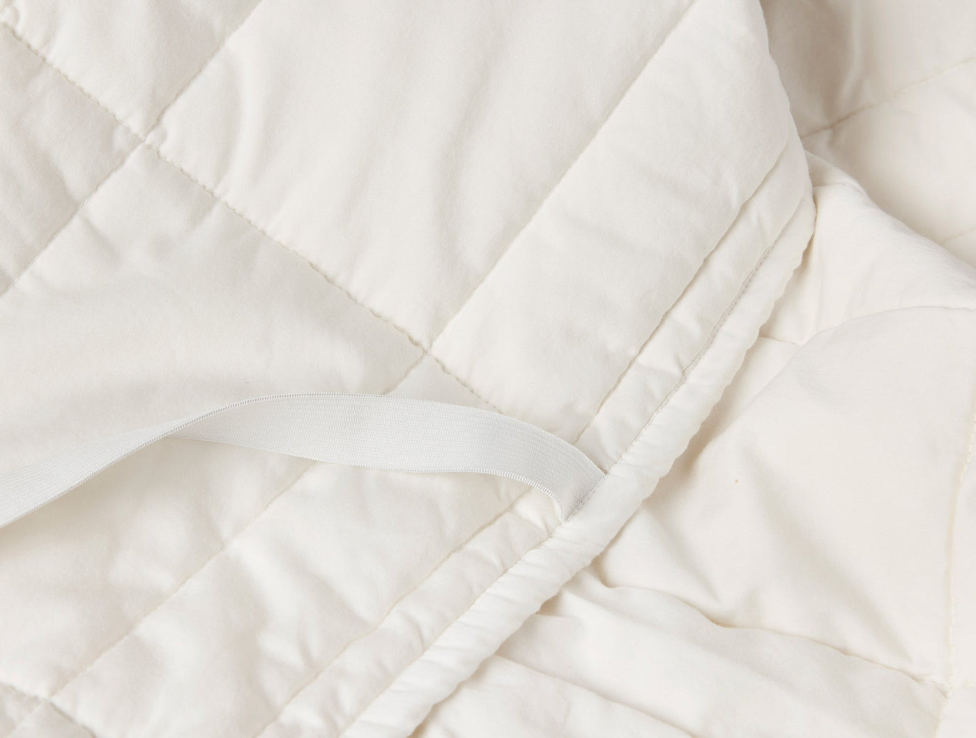 Close-up of ivory quilted mattress topper showing tie strap and stitched panel detail.
