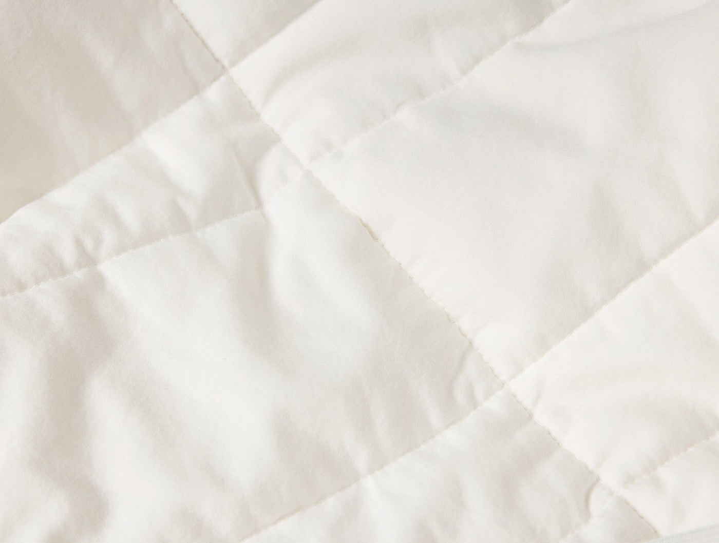Close-up of ivory quilted cotton fabric showing diagonal stitching pattern and soft fill.