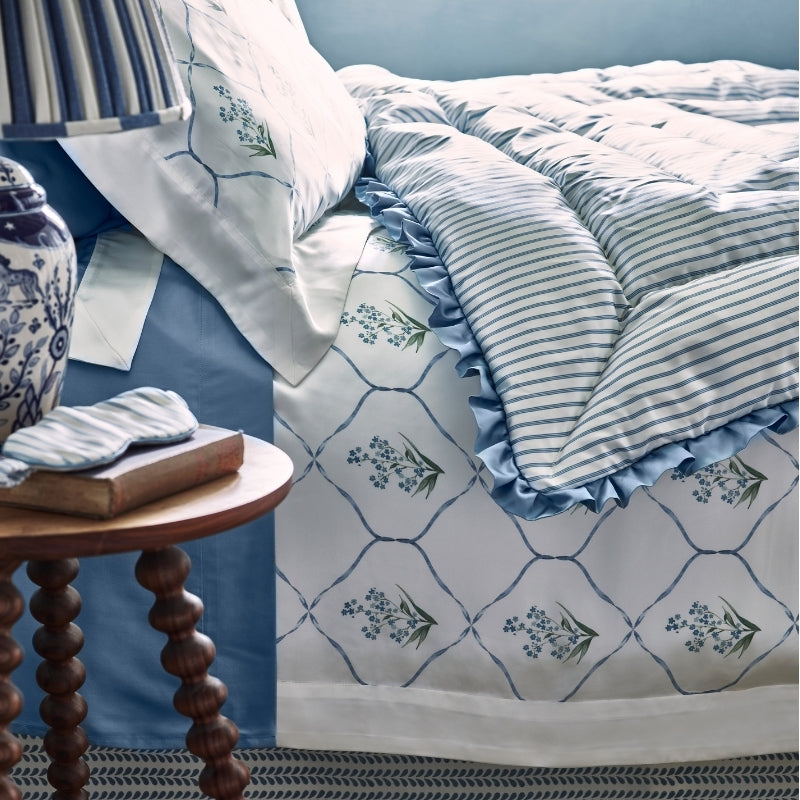 Angled view of blue floral lattice silk duvet layered with striped ruffle throw on styled bed.
