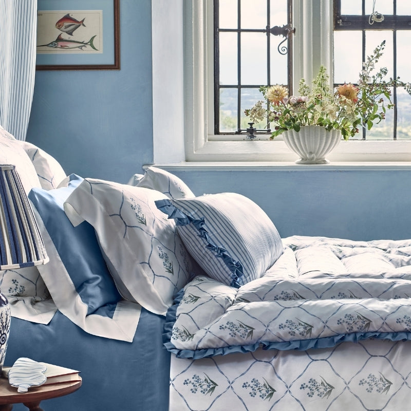 Forget Me Not duvet cover styled on bed with ruffled edges and blue floral motifs.