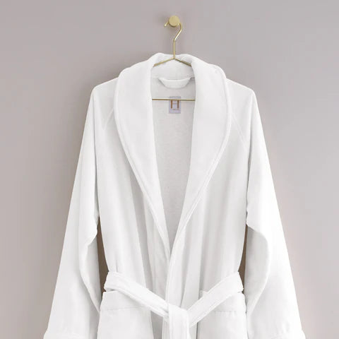 The Shawl Collar Robe by Frette, featuring a soft texture and belt, hangs on a gold hook against a plain light gray wall.