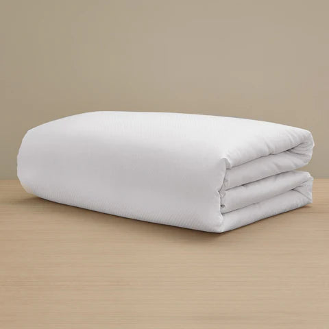 The Checkered Sateen Duvet Cover by Frette, crafted from silky fabric, is neatly folded and displayed on a light wooden surface with a plain beige background.