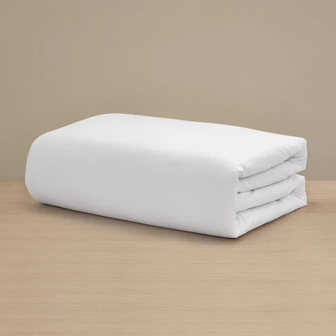 The Frette Percale Duvet Cover by Frette, crafted from 100% cotton, is neatly folded and displayed on a light wooden surface with a beige background.