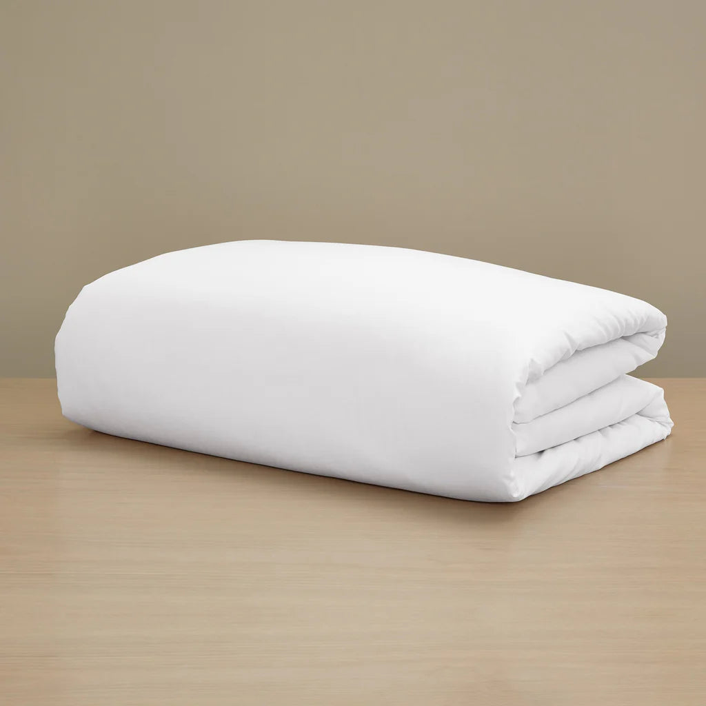 The Frette Sateen Duvet Cover by Frette, with a luxurious white finish, is neatly folded and displayed on a light wooden surface against a plain beige background.