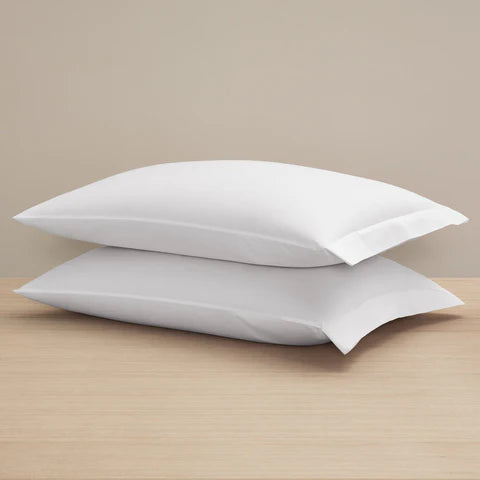 Two Frette Sateen Pillowcase Sets by Frette are stacked on a wooden surface against a beige background, ideal for pairing with luxury bedding or a crisp 100% cotton duvet cover.