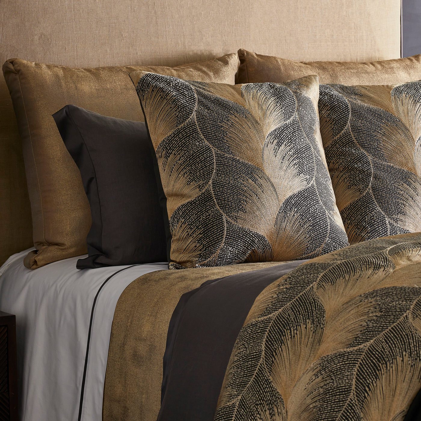 Styled bed showing gold and charcoal Fan duvet with bold botanical leaf pattern.