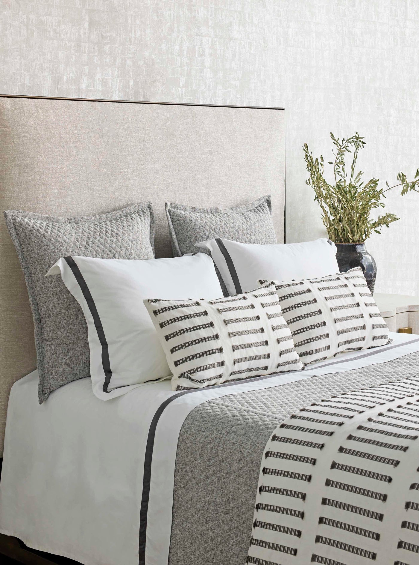 Styled bedroom with grey textured coverlet, mixed pillows in white and charcoal stripe patterns.