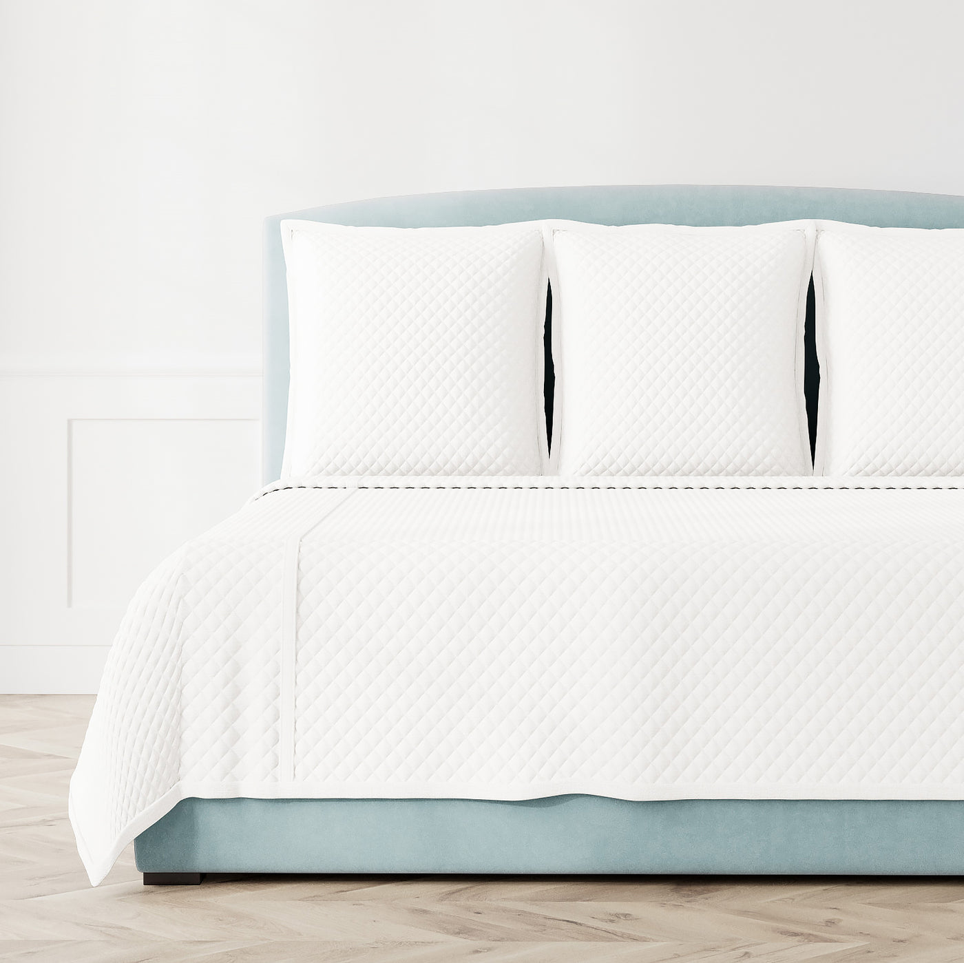 White quilted coverlet set on bed with diamond texture pattern and three matching shams.