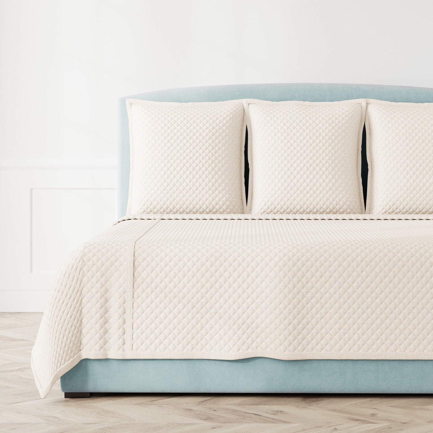 Ivory quilted diamond-pattern coverlet set styled on a bed with matching shams.