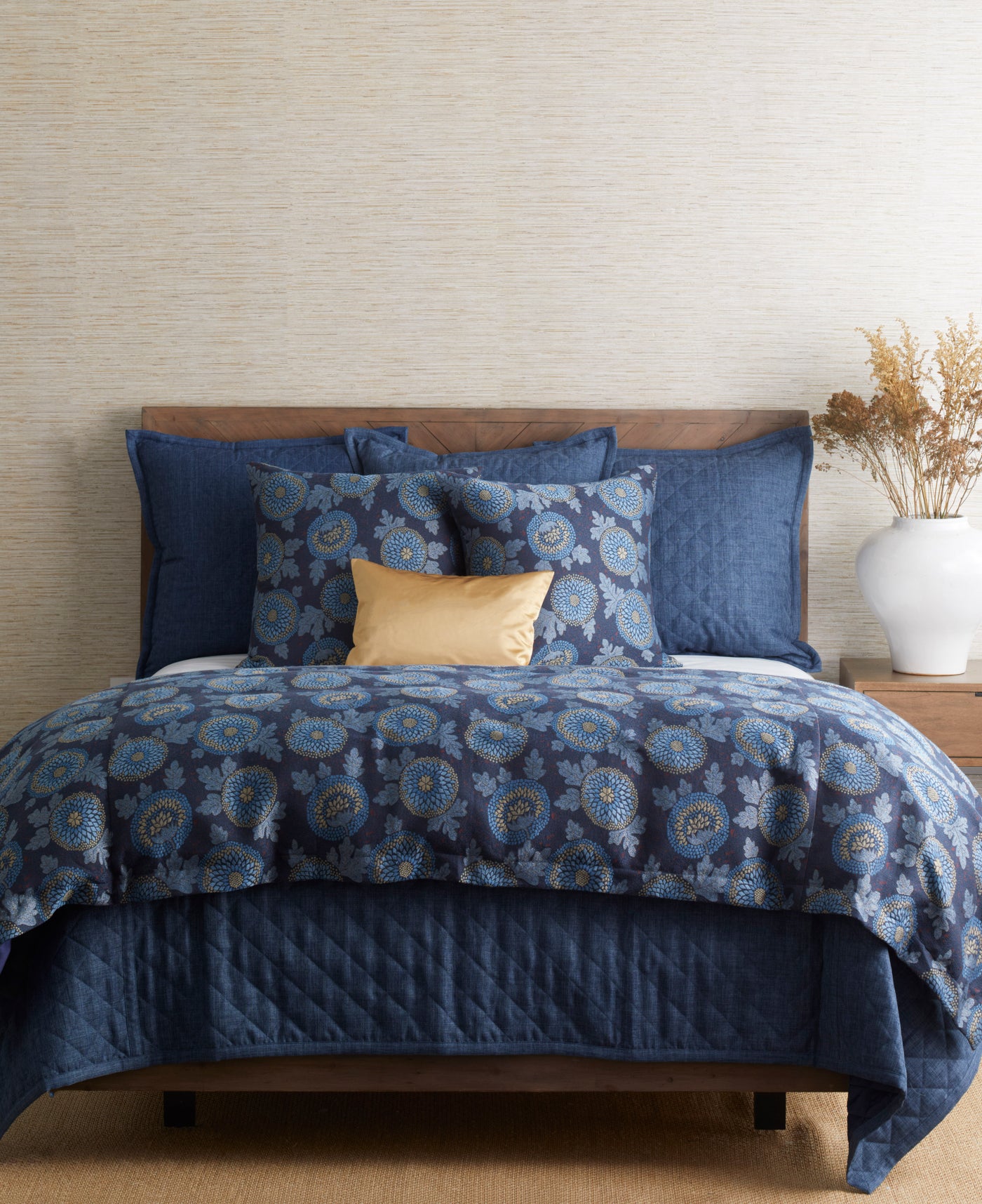 Navy quilted linen coverlet set on made bed with floral medallion pillows and gold accent pillow.