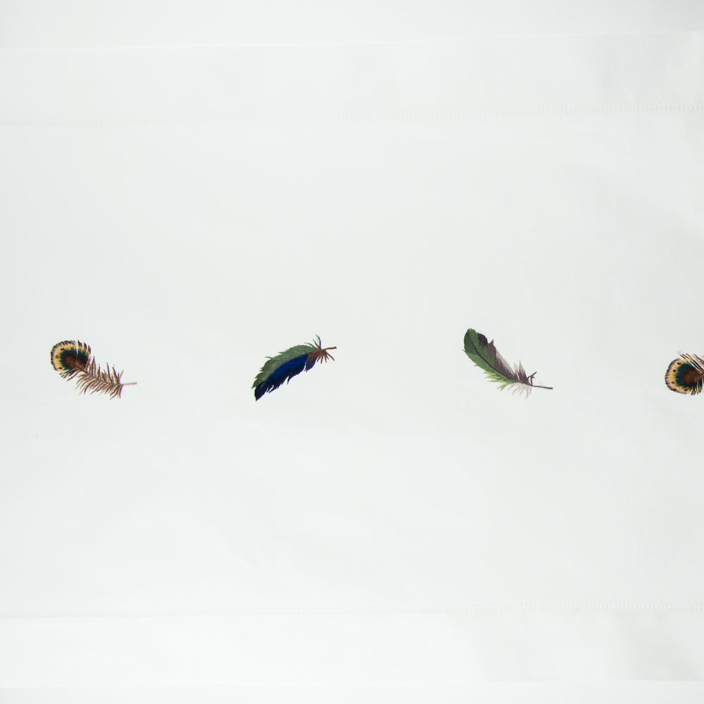 Close-up of embroidered peacock and iridescent feather motifs along ivory linen table runner hem.