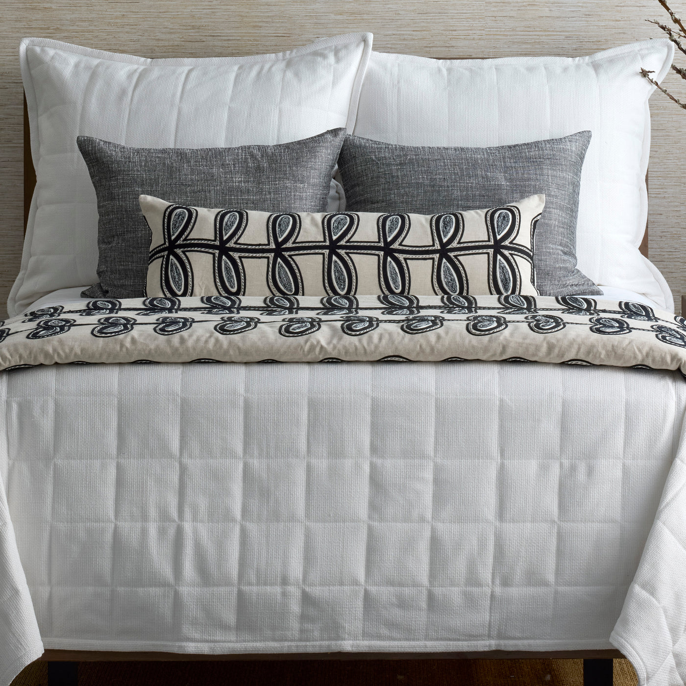 Ivory lumbar pillow with black loop embroidery displayed on a white quilted bed.