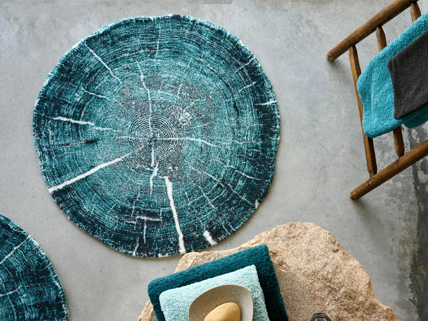 Abyss Habidecor Fossile bath rug in teal, circular tree ring pattern on grey surface.