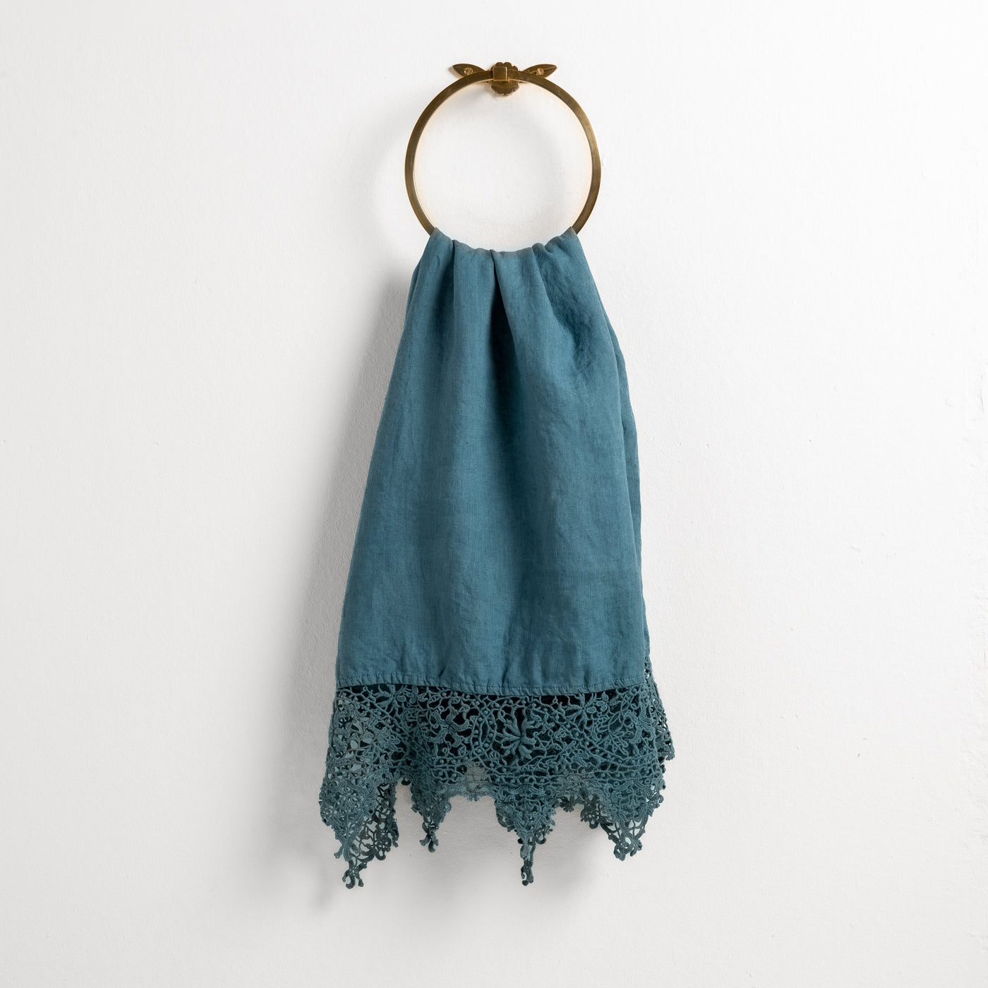 Cenote linen guest towel with crochet lace hem, draped on a brass ring towel holder.