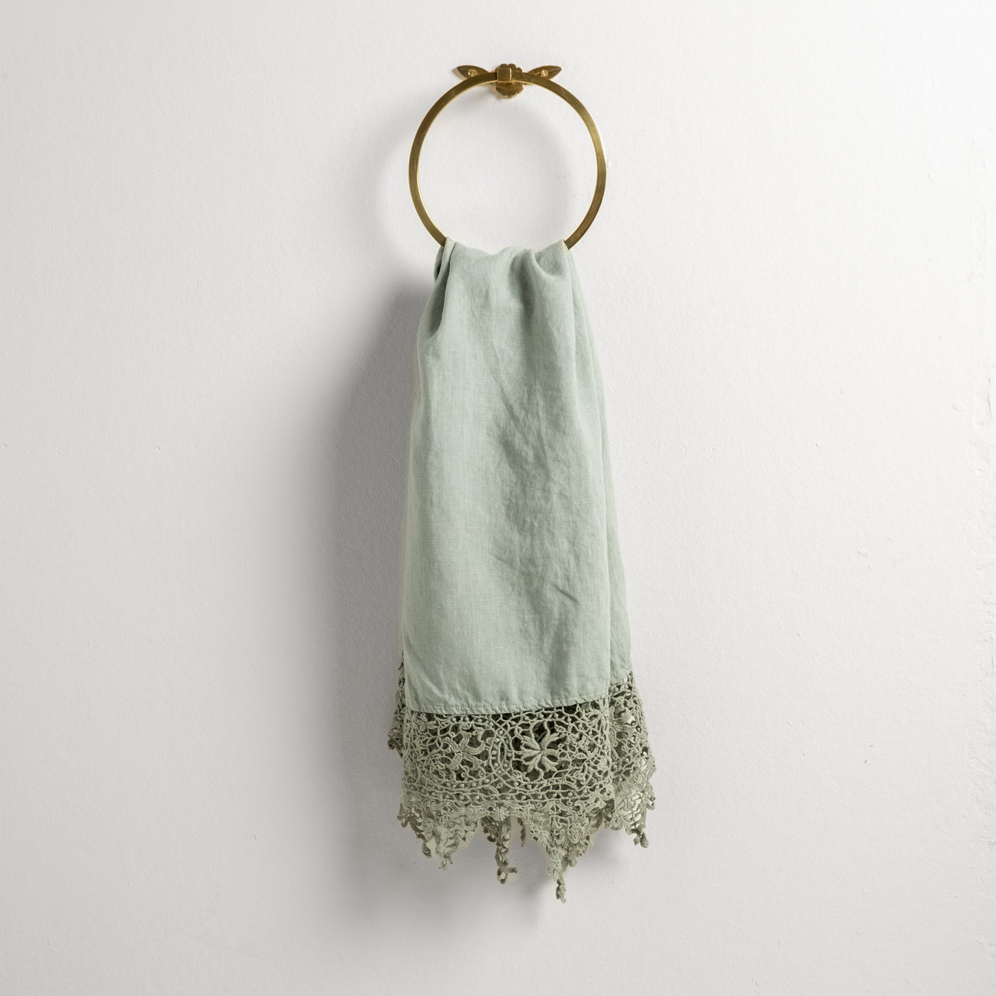 Eucalyptus guest towel draped on gold ring, showing floral crochet lace trim and tassel fringe hem.