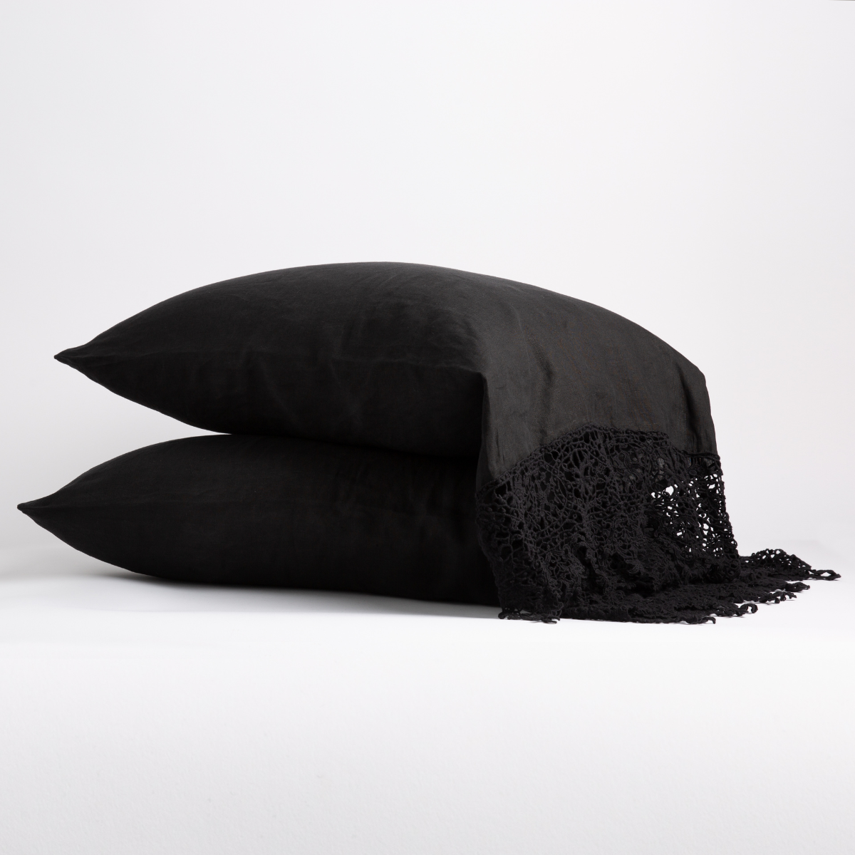 Two stacked Corvino linen pillowcases with macramé fringe trim detail at corner.