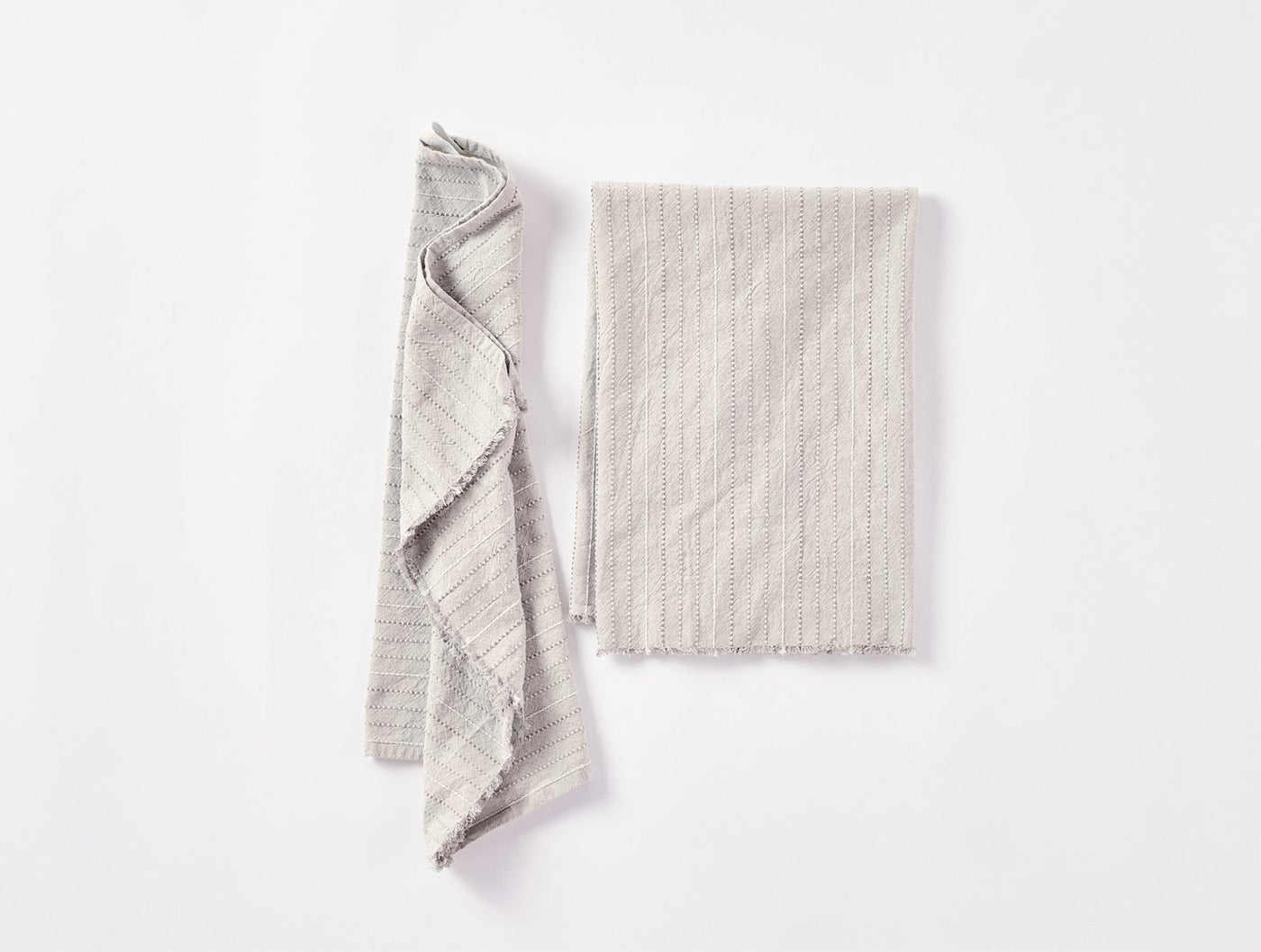 Pair of Coyuchi Fringe Stripe hand towels in natural, one folded, one draped.