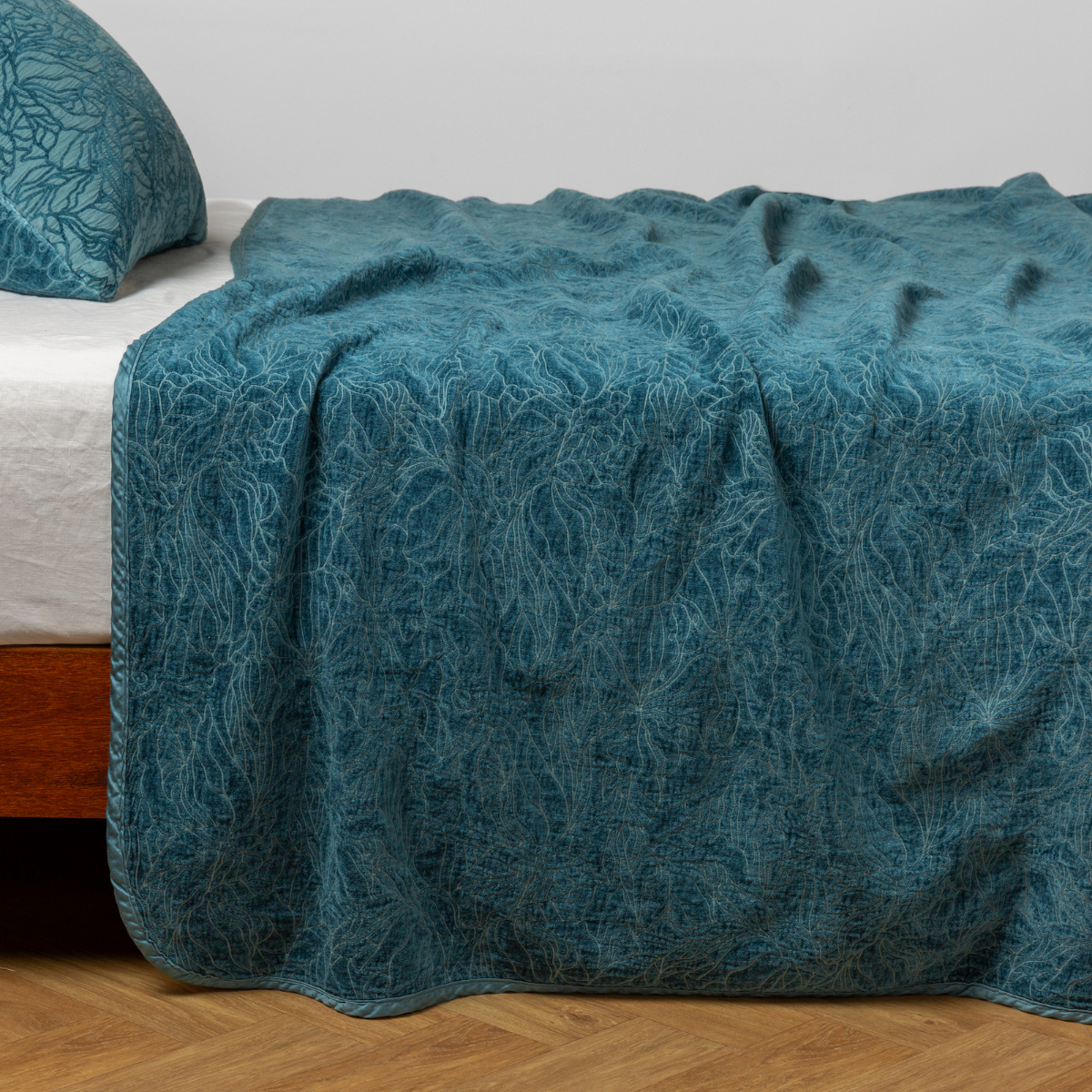 Bella Notte Georgia bedspread in Cenote draped over bed, teal botanical jacquard pattern.