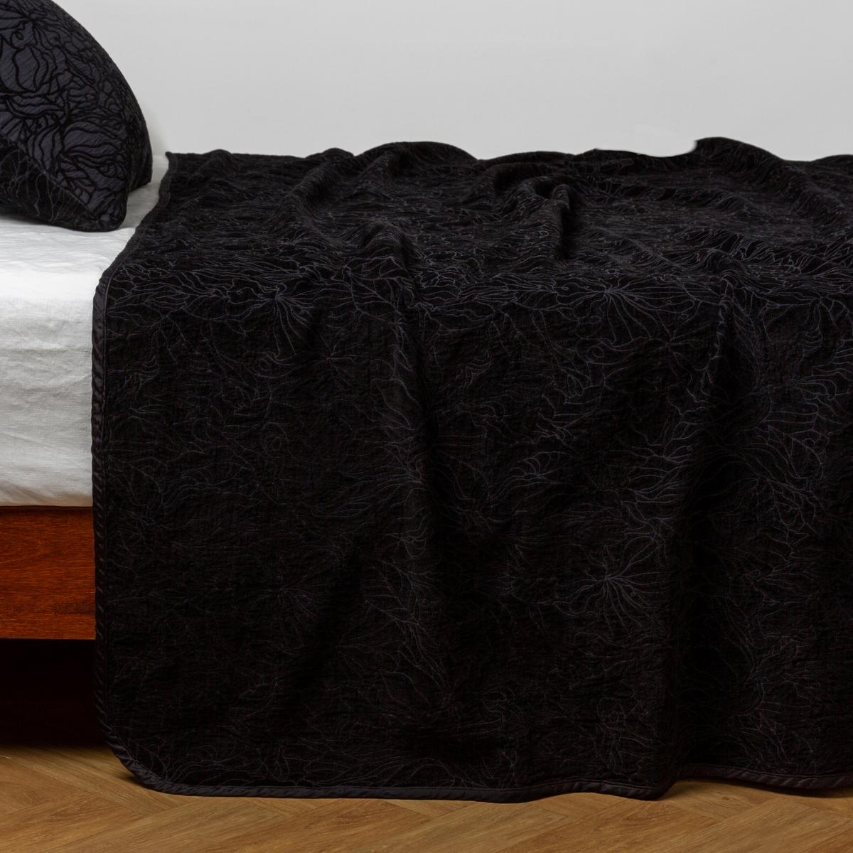 Black floral-embossed Corvino bedspread draped over bed corner, matching pillow visible.