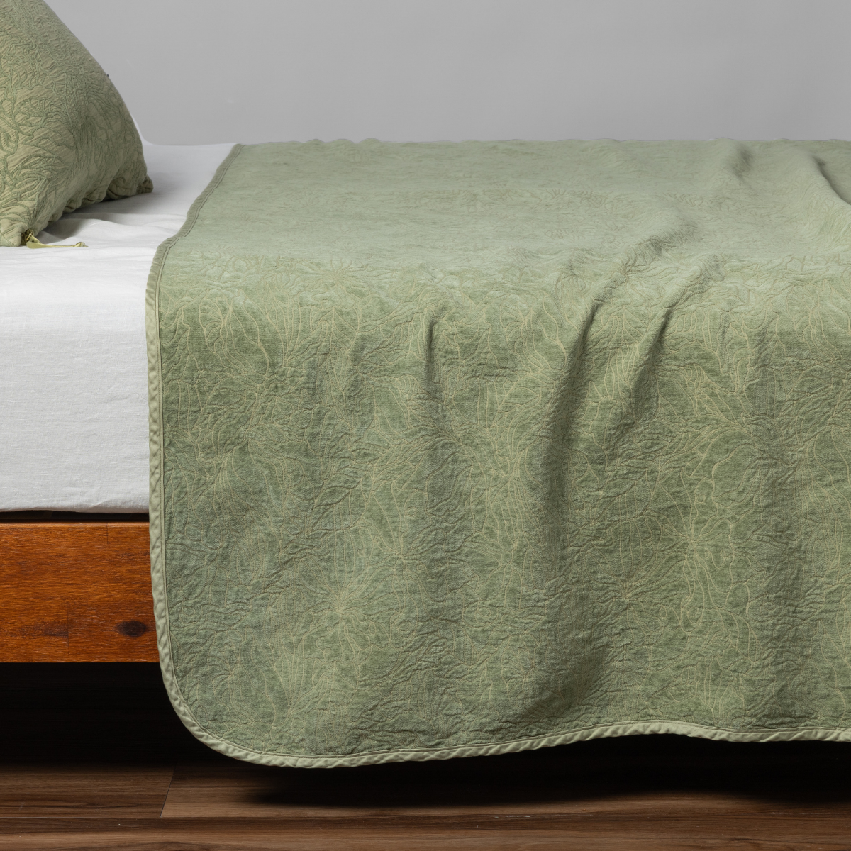 Desert Sage bedspread draped over bed corner, showing quilted botanical texture and scalloped edge.