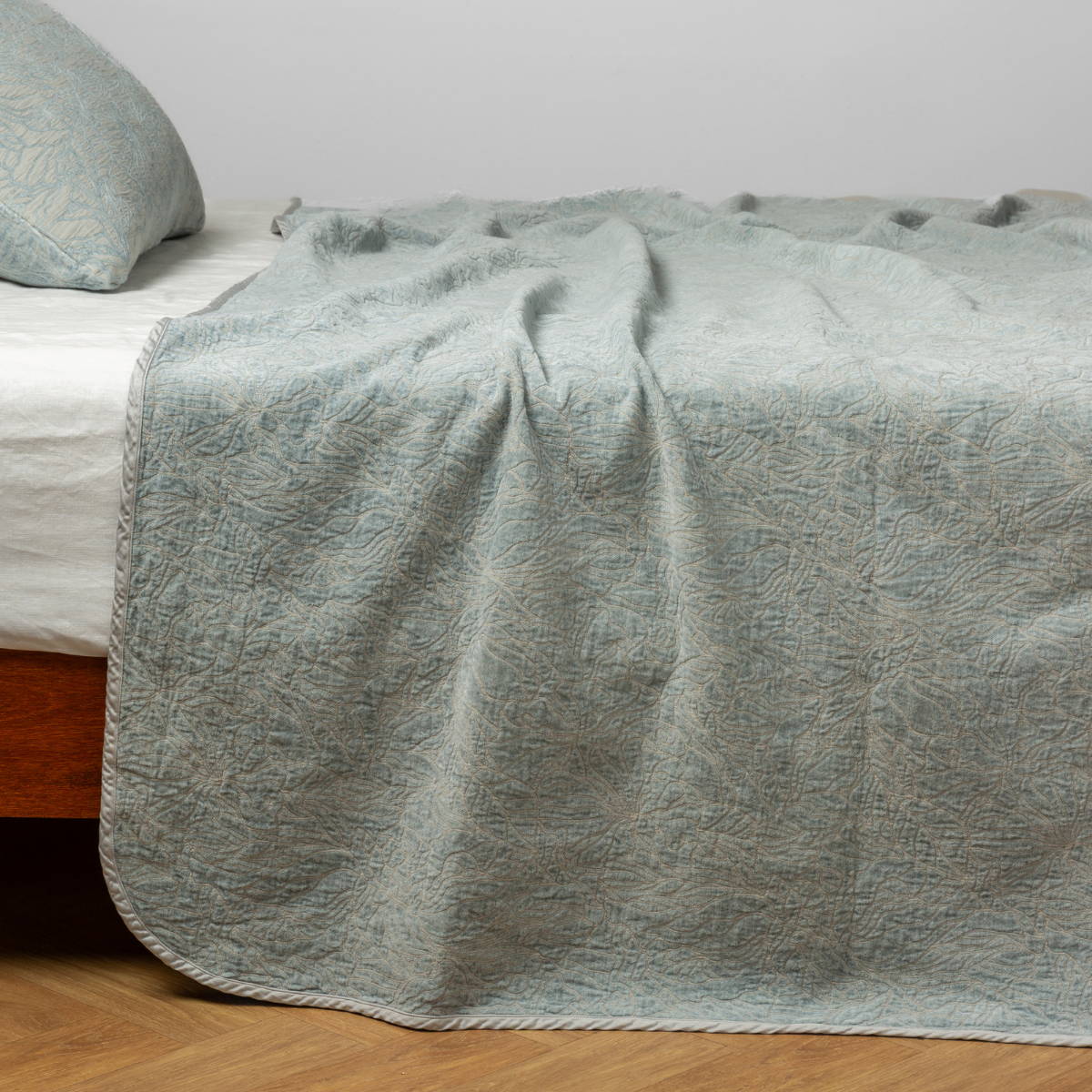 Eucalyptus quilted bedspread draped over bed corner, showing floral stitching detail.